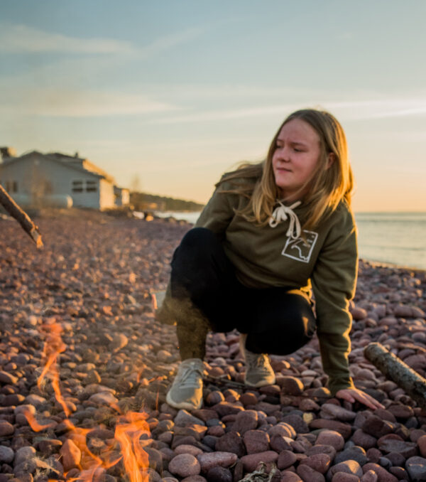 Young girl wearing military green hoodie next a fire on lake superior