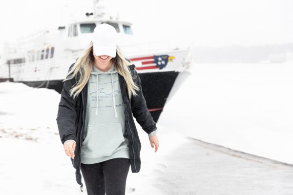 Young lady wearing a blue hoodie with a jacket in front of a boat