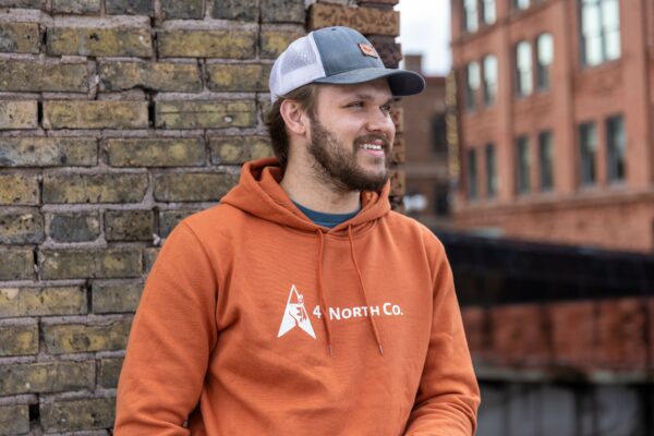 Young man wearing a copper hoodie next to a brick building