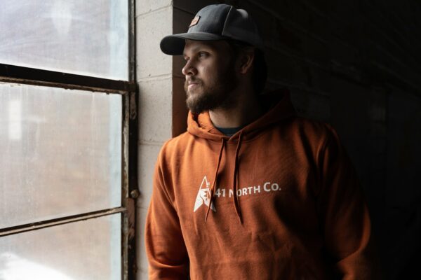 Young man wearing copper hoodie next to a window